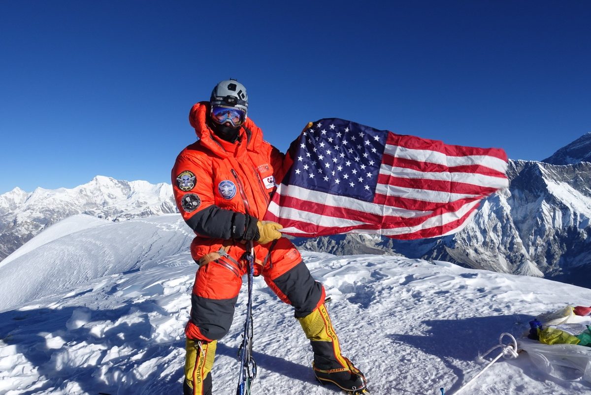 Mark Parella holding an American flag on the summit of Ama Dablam in 2021, with Himalayan peaks behind